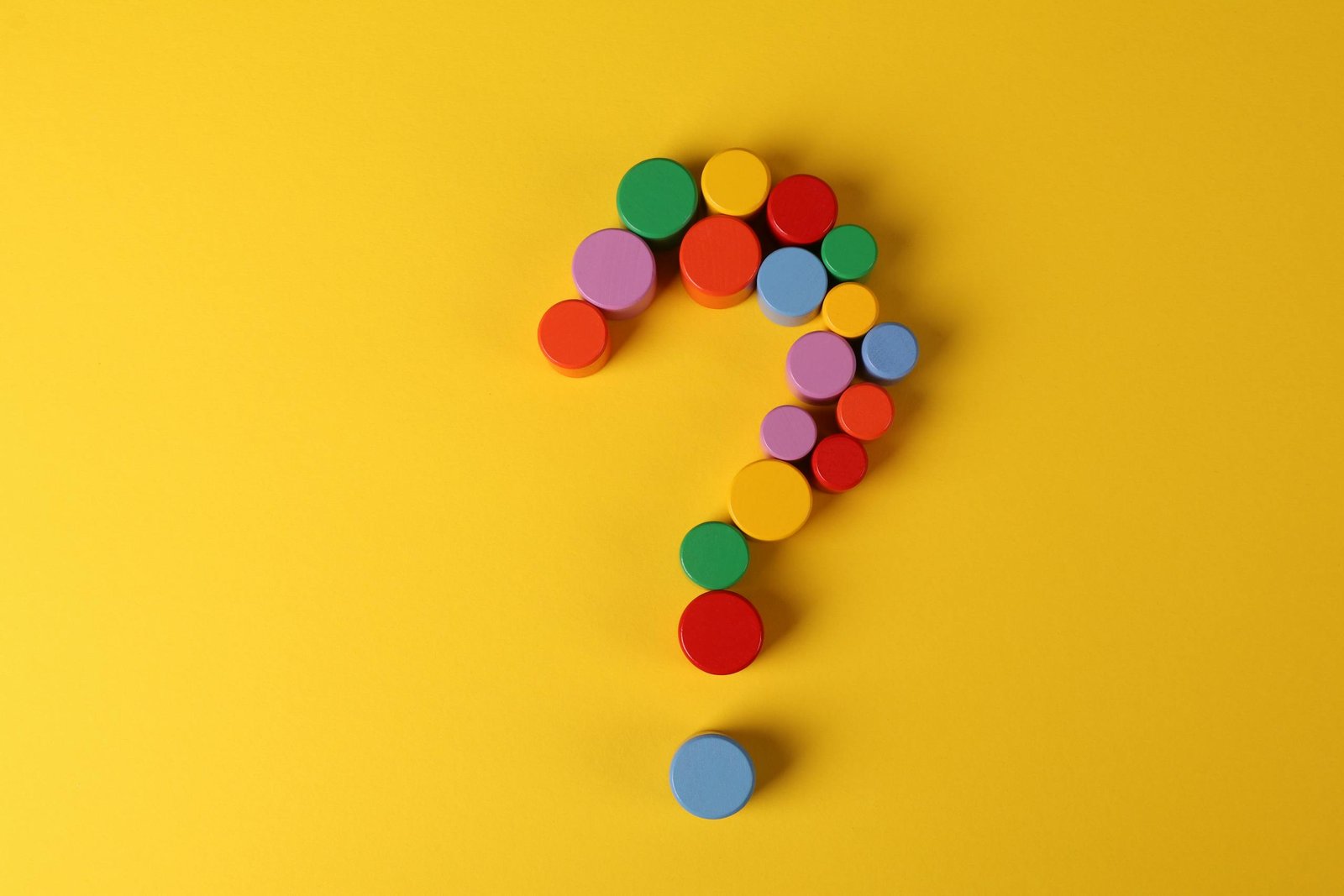 A vibrant question mark made from colorful circular blocks on a yellow background, symbolizing curiosity and inquiry.